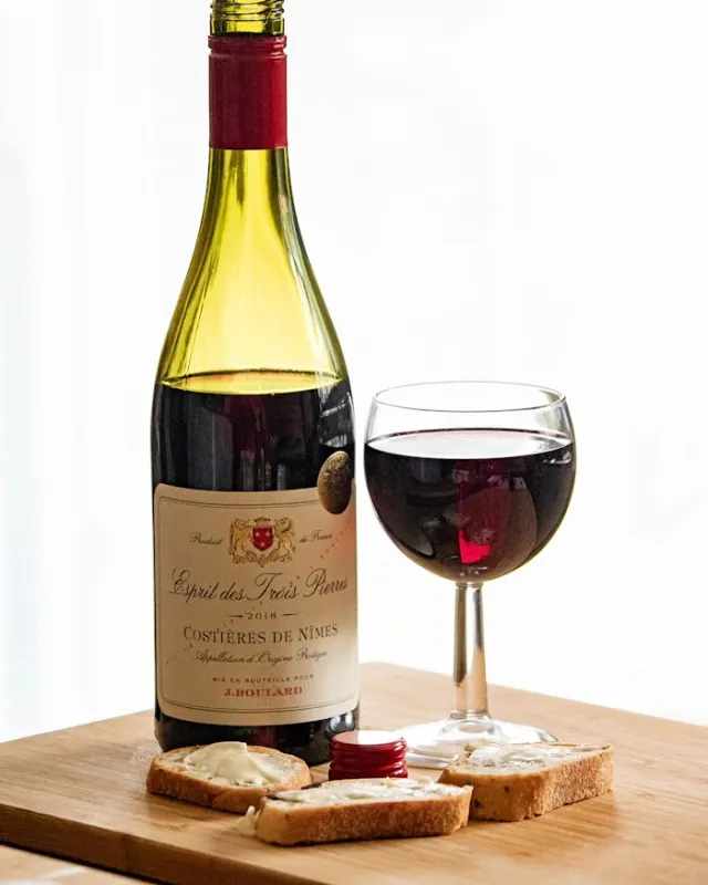 Garrafa de vinho tinto e taça sobre tábua de madeira na Adega Monteiro